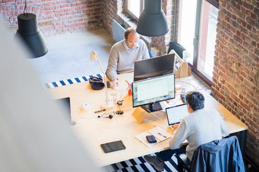 Bird's-eye view of a modern office with professionals collaborating on laptops and monitors.